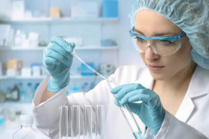 Frau in Laborkleidung mit Pipette und Reagenzglas